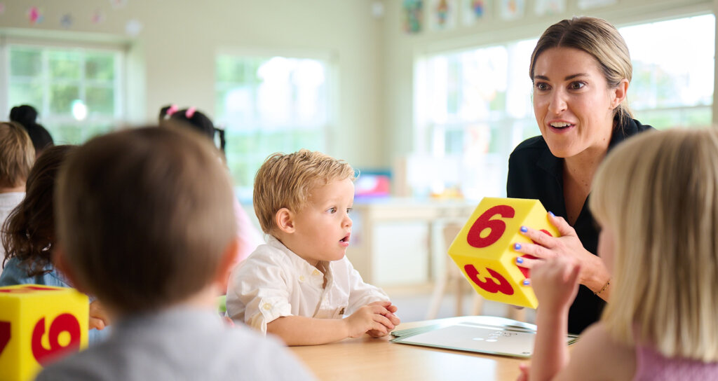 Primrose teacher leading a math lesson, showing children a block with numbers on it